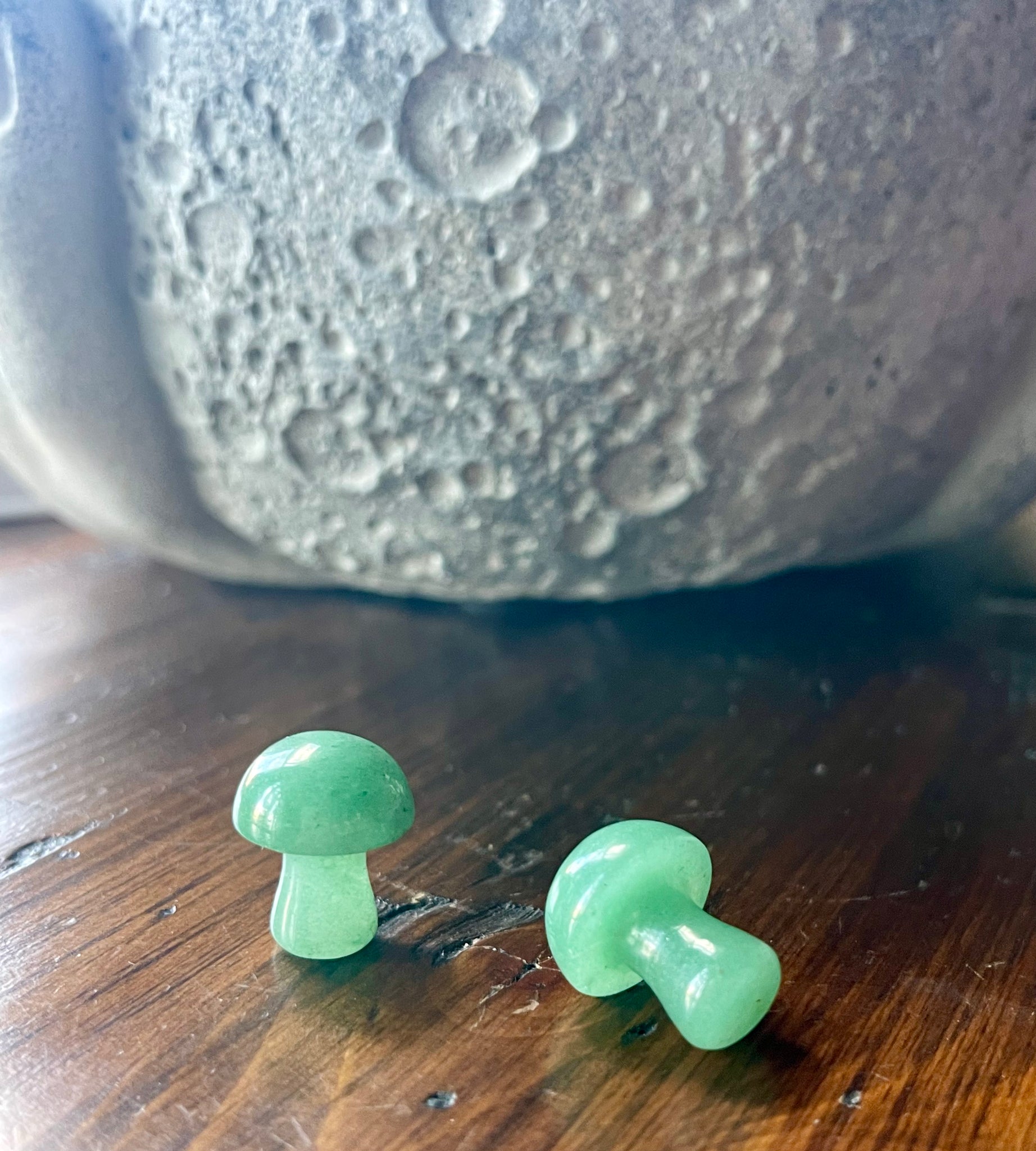 Kelowna Crystal Cave - Two green glass mushroom-shaped objects on a wooden surface with a textured gray background.