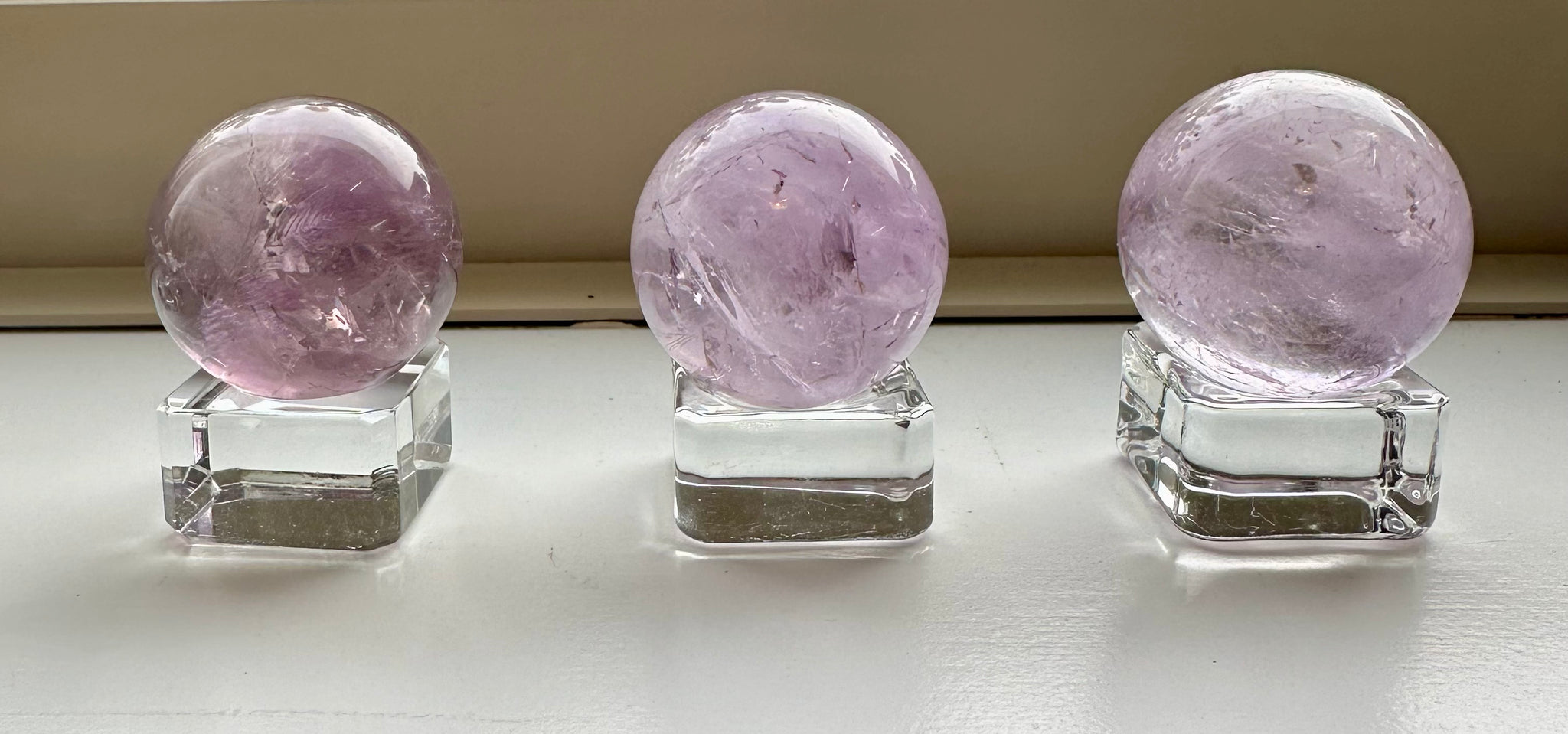 Kelowna Crystal Cave - Amethyst Spheres on display, with a purple hue, intended as decorative or healing stones, placed on clear stands.
