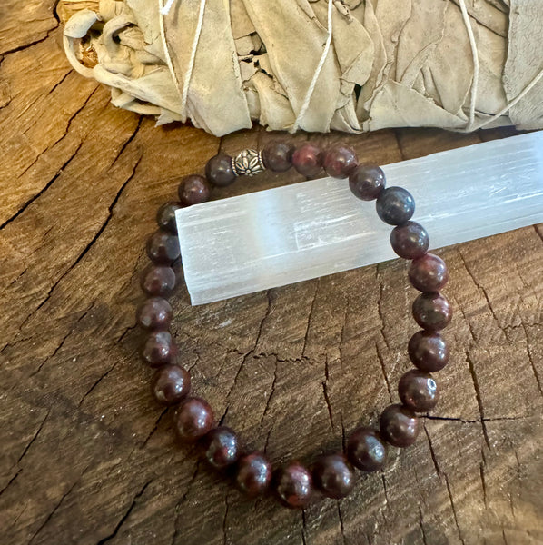 My Two Daughters Jewelry - A bloodstone bracelet with round beads, displayed on a wooden surface next to a white crystal.
