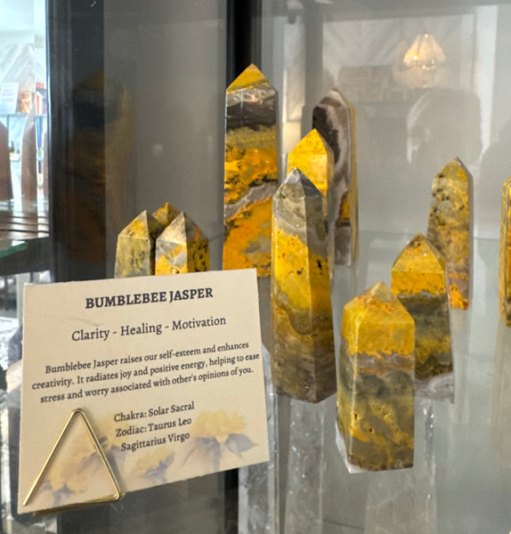 Kelowna Crystal Cave - A display of Bumblebee Jasper crystal points in a glass case, with a descriptive card in front reading 'BUMBLEBEE JASPER' and listing chakra, elemental, and zodiac associations.