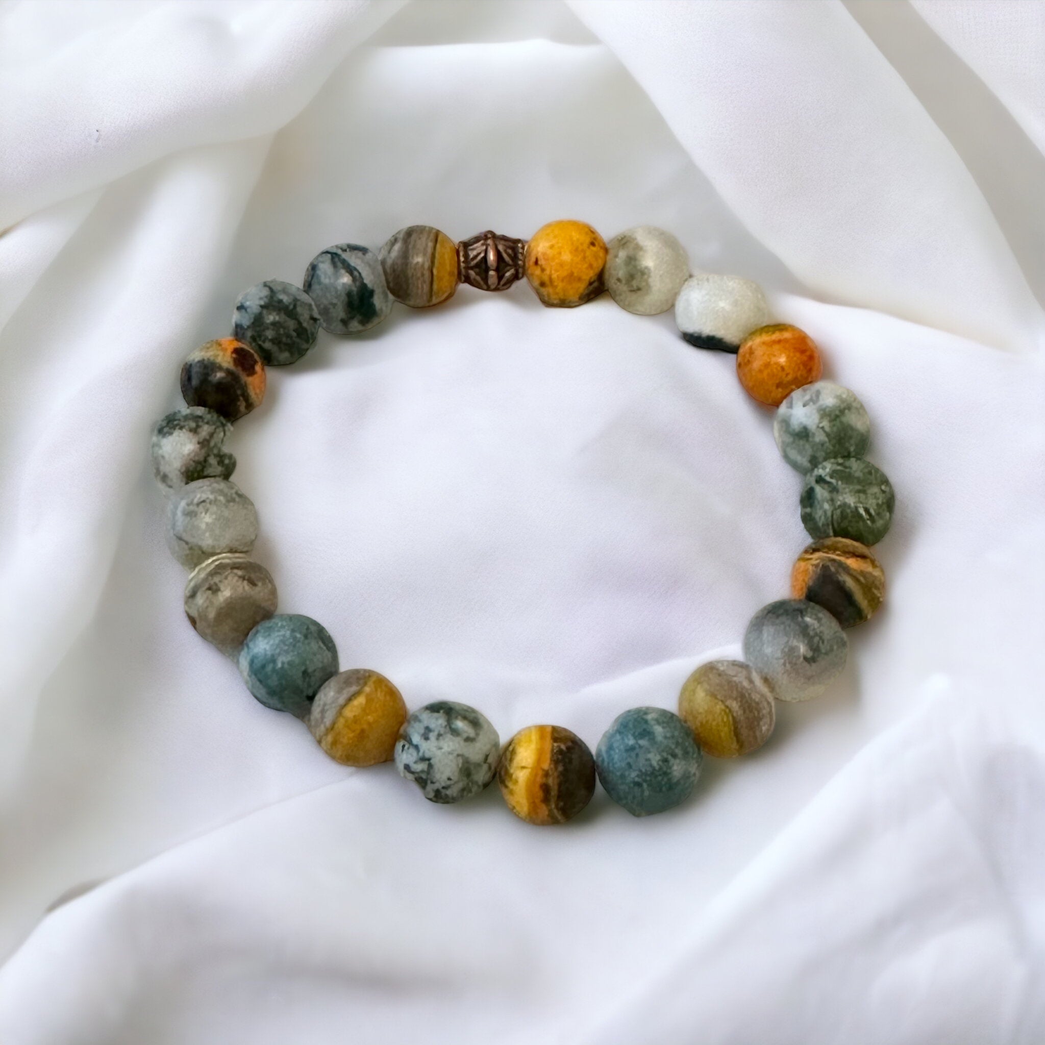 My Two Daughters Jewelry - A bracelet made of round beads, featuring various colors including white, yellow, and gray, displayed on a white fabric surface.