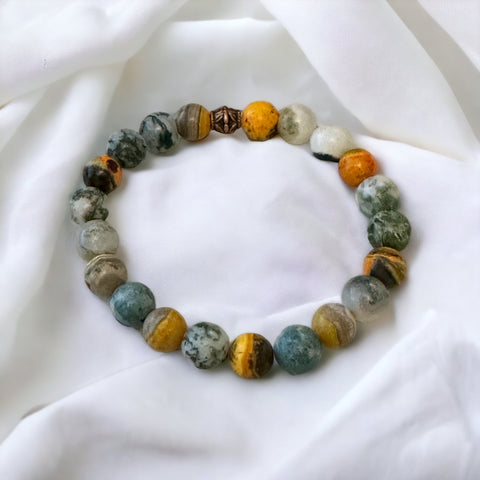 My Two Daughters Jewelry - A bracelet made of round beads, featuring various colors including white, yellow, and gray, displayed on a white fabric surface.
