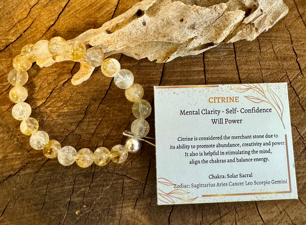 My Two Daughters Jewelry - A citrine bracelet displayed alongside a wooden piece, with a card detailing the properties of citrine, including mental clarity, self-confidence, and will power.