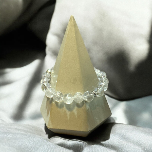 My Two Daughters Jewelry - A clear quartz bracelet displayed on a triangular stand, with the bracelet composed of multiple transparent crystals linked together.