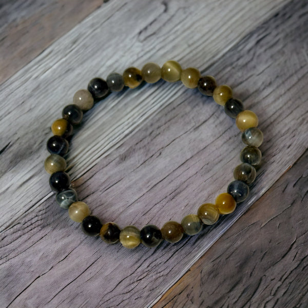 My Two Daughters Jewelry - A bracelet made of round beads with varying shades of brown and black, laid out on a wooden surface.