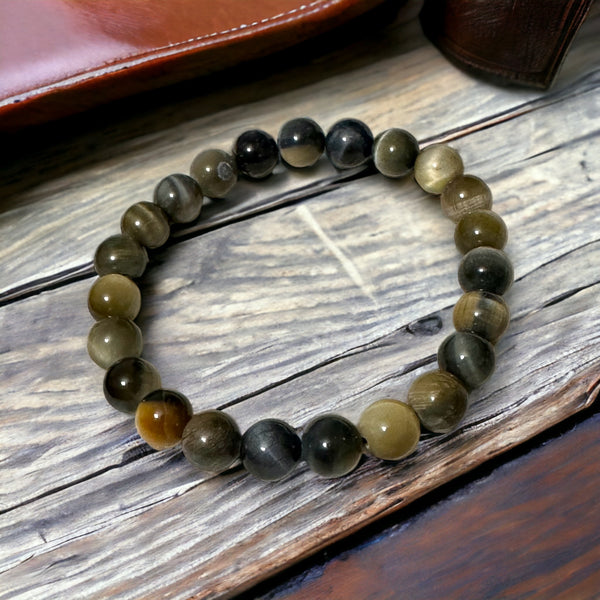 My Two Daughters Jewelry - A bracelet made of round beads with varying shades of brown and black, laid out on a wooden surface.