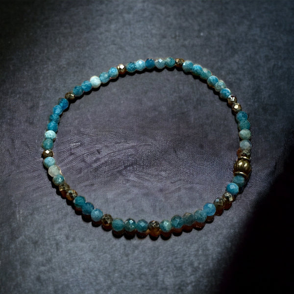 My Two Daughters Jewelry - A faceted bracelet made of Apatite stone beads, displayed on a white fabric surface.