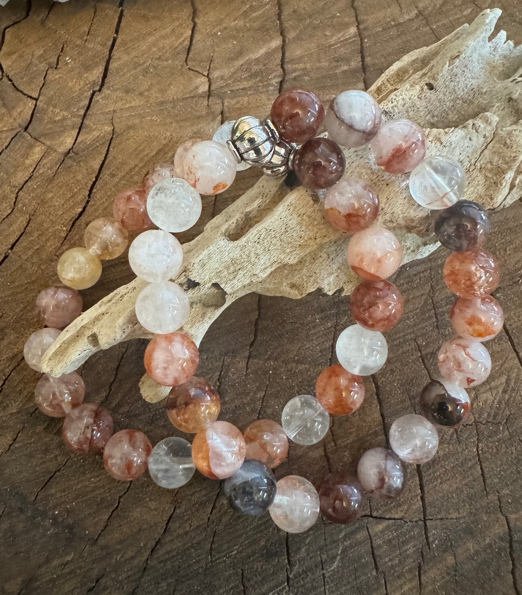 My Two Daughters Jewelry - A multicolored fire quartz bracelet with a silver clasp, displayed on a wooden surface with a piece of quartz crystal in the background.