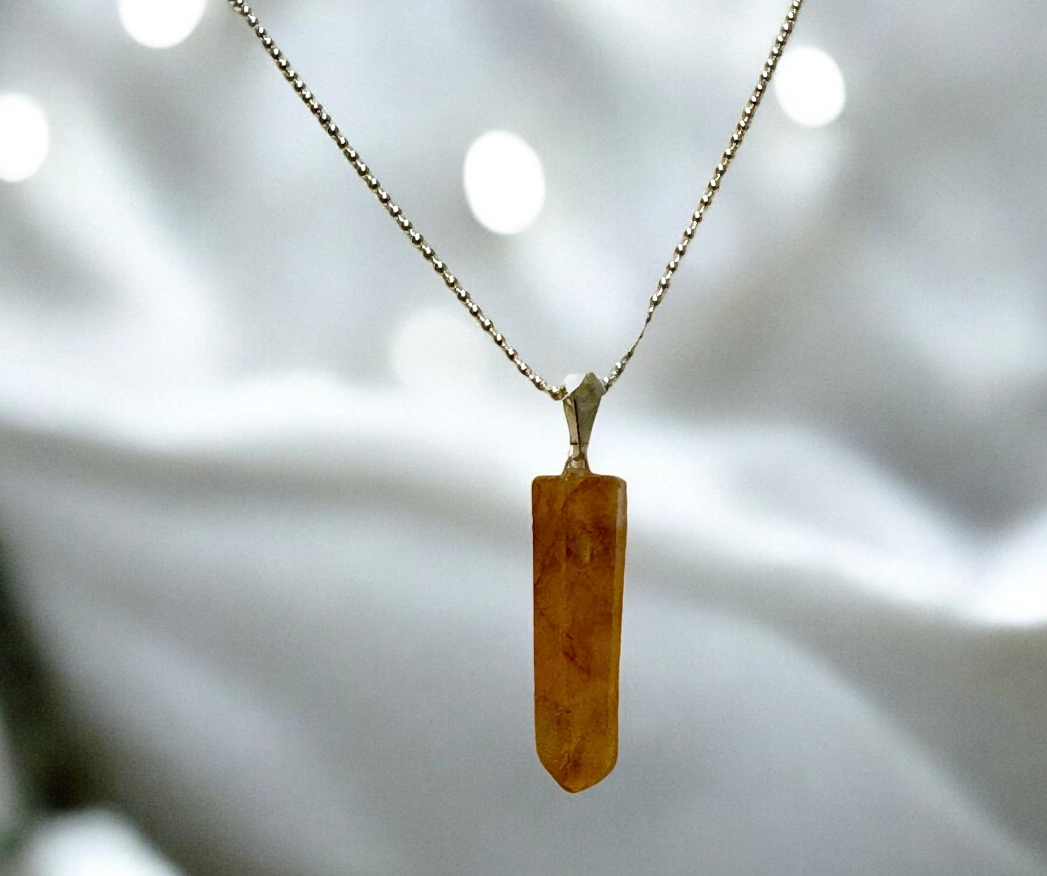 My Two Daughters Jewelry - A Golden Healer crystal pendant point attached to a gold-colored chain, with the necklace displayed against a blurred white background.
