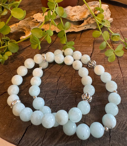My Two Daughters Jewelry - A bracelet made of green angelite stones, with a decorative silver clasp, displayed on a wooden surface with foliage in the background.
