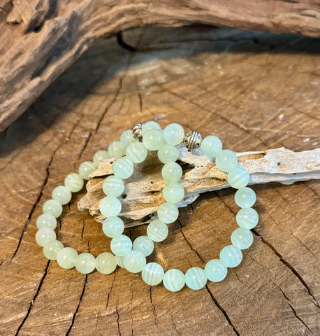 My Two Daughters Jewelry - A green calcite bracelet displayed on a wooden surface with a piece of driftwood in the background.
