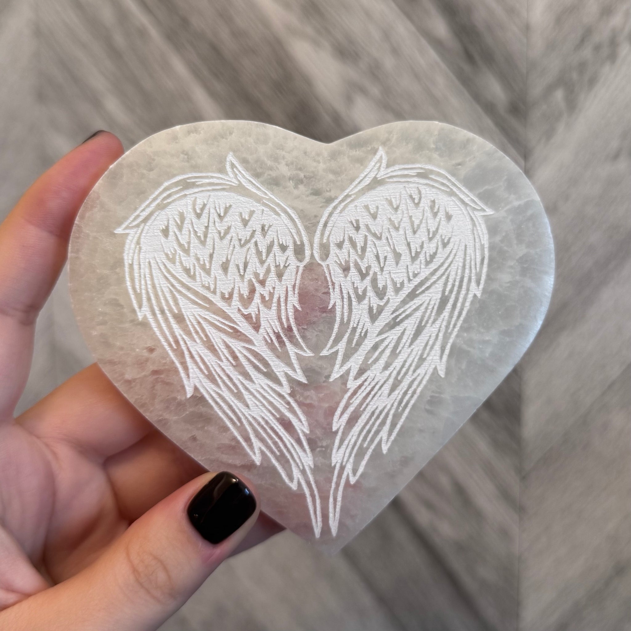 Kelowna Crystal Cave - Heart-shaped stone with angel wings engraving held by a hand on a wooden surface