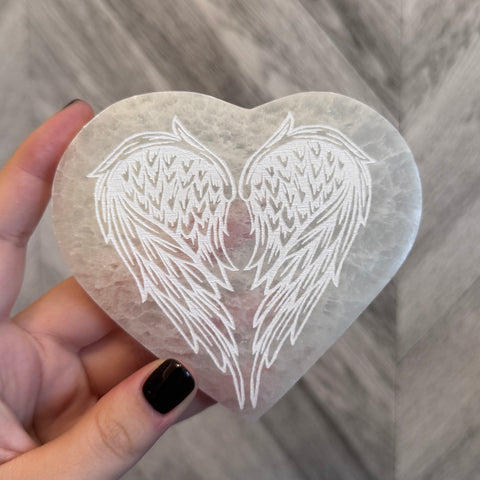 Kelowna Crystal Cave - Heart-shaped stone with angel wings engraving held by a hand on a wooden surface