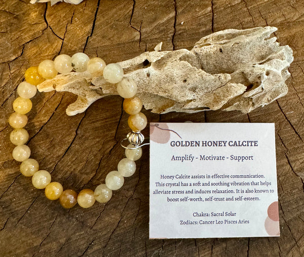 My Two Daughters Jewelry - A honey calcite bracelet displayed on a wooden surface, with a decorative tag indicating the product name and properties.