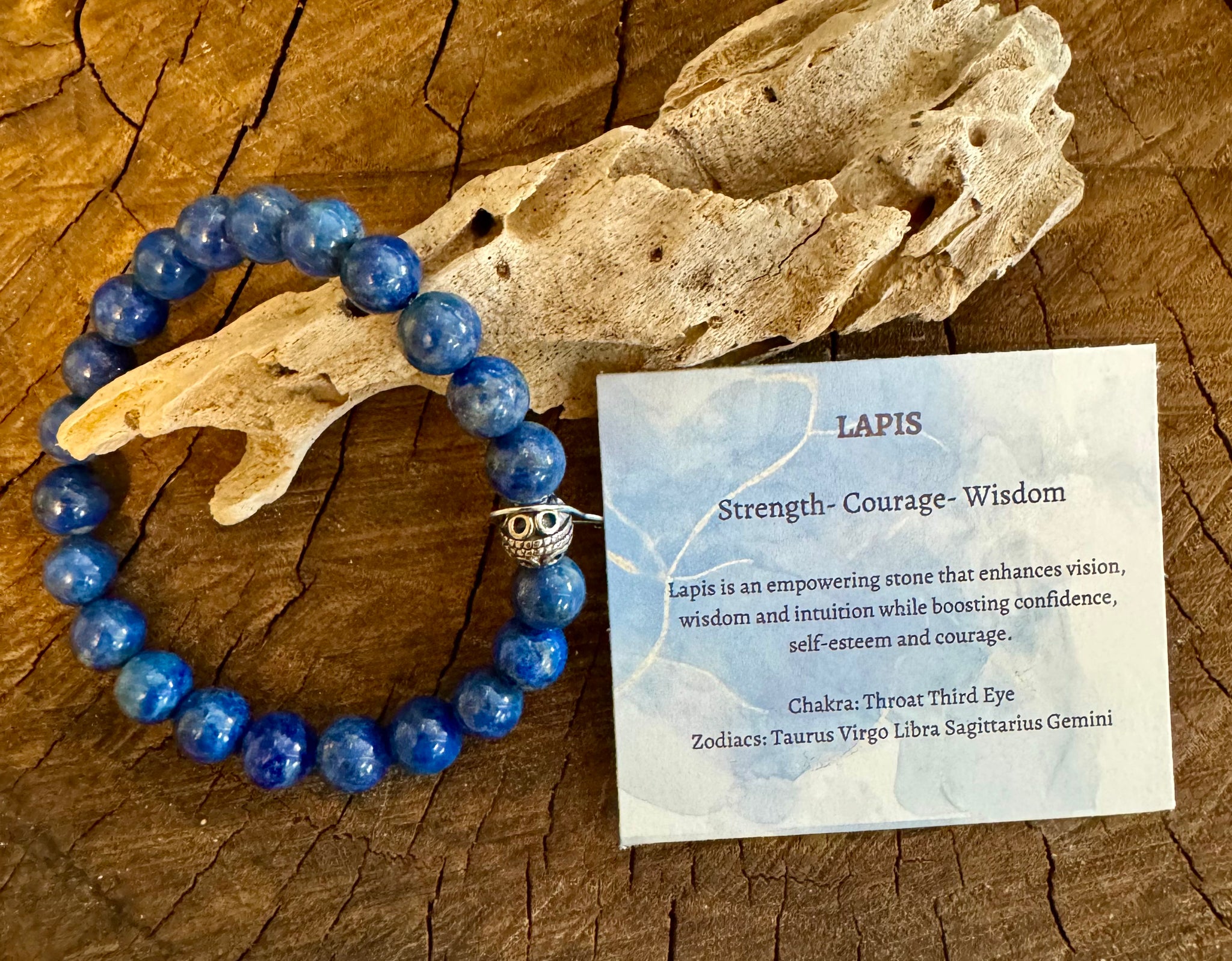 My Two Daughters Jewelry - A blue Lapis Lazuli Bracelet displayed alongside a wooden piece and a card explaining the properties of the stone, placed on a wooden surface.
