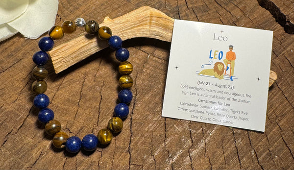 My Two Daughters Jewelry - Bracelet with blue and brown beads on a wooden surface next to a card about Leo zodiac sign.