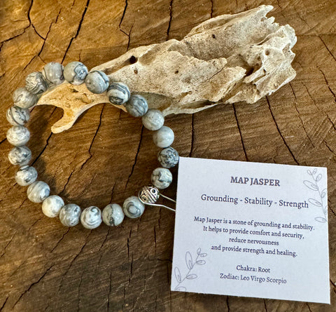 My Two Daughters Jewelry - A Map Jasper bracelet displayed on a wooden surface, with a card detailing the properties of the stone, including grounding, stability, and strength.