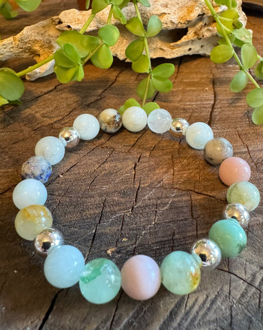 My Two Daughters Jewelry - A bracelet with round beads in shades of green, blue, and pink, with metallic silver accents, displayed on a wooden surface with foliage in the background.