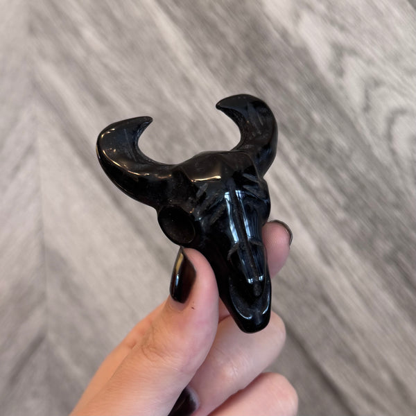 Kelowna Crystal Cave - Black decorative item shaped like a bull's head held by a hand on a wooden surface