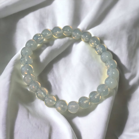 My Two Daughters Jewelry - A bracelet made of round opalite beads, displayed on a white fabric surface.