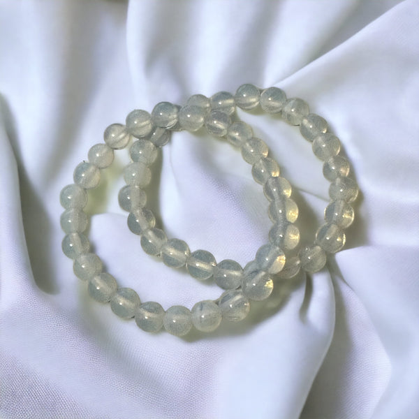 My Two Daughters Jewelry - A bracelet made of round opalite beads, displayed on a white fabric surface.