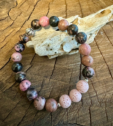 My Two Daughters Jewelry - A bracelet made with round beads of varying shades of pink, brown, and black, displayed on a wooden surface.