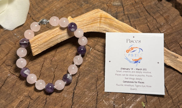 My Two Daughters Jewelry - Beaded bracelet with purple and white stones on a wooden surface next to a card with astrological information.