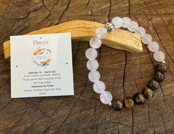 My Two Daughters Jewelry - A colorful bracelet made of rose quartz and tigers Eye stones, displayed on a wooden surface, with a card indicating the Pisces zodiac sign and properties of the gemstones.