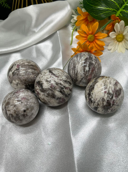 Kelowna Crystal Cave - A collection of polished pink tourmaline spheres placed on a smooth surface with a floral arrangement and a white fabric in the background.