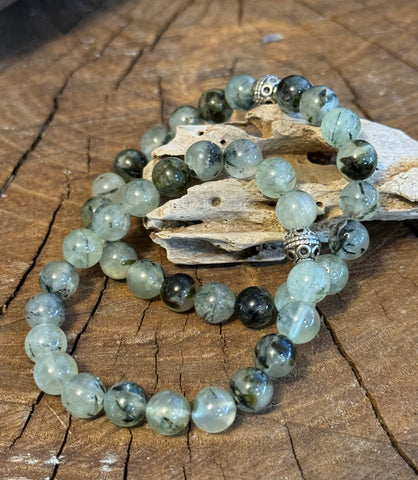 My Two Daughters Jewelry - A prehnite bracelet with green beads and silver-colored accents placed on a wooden surface.