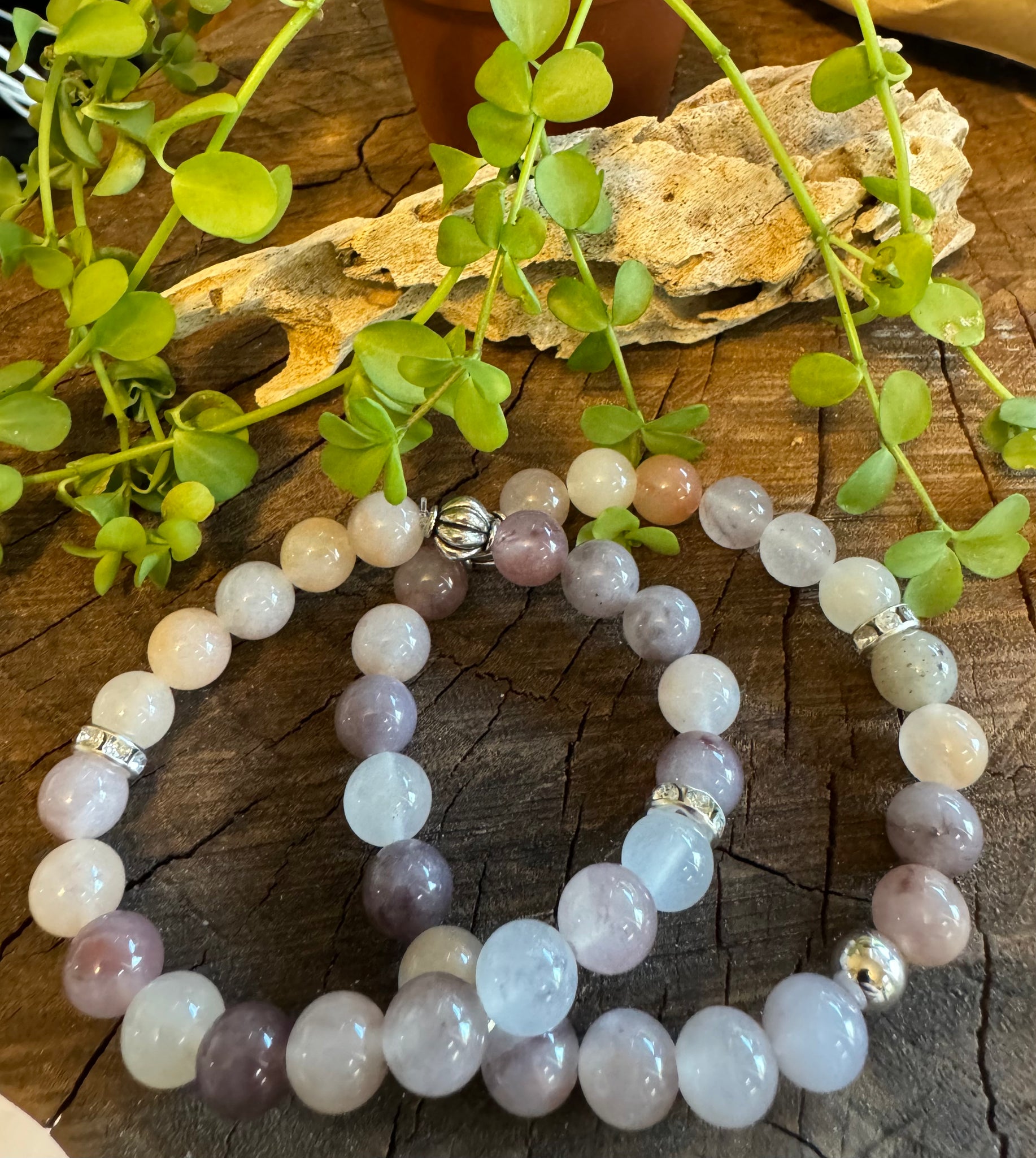 My Two Daughters Jewelry - A bracelet made with purple and translucent beads, featuring metallic accents, displayed on a wooden surface with green leaves in the background.