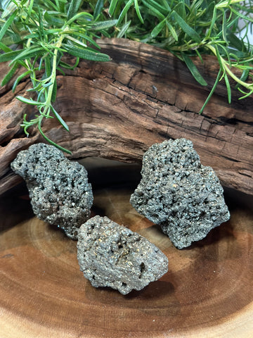 Kelowna Crystal Cave - Several natural chunks of pyrite displayed on a wooden surface with a green plant in the background.