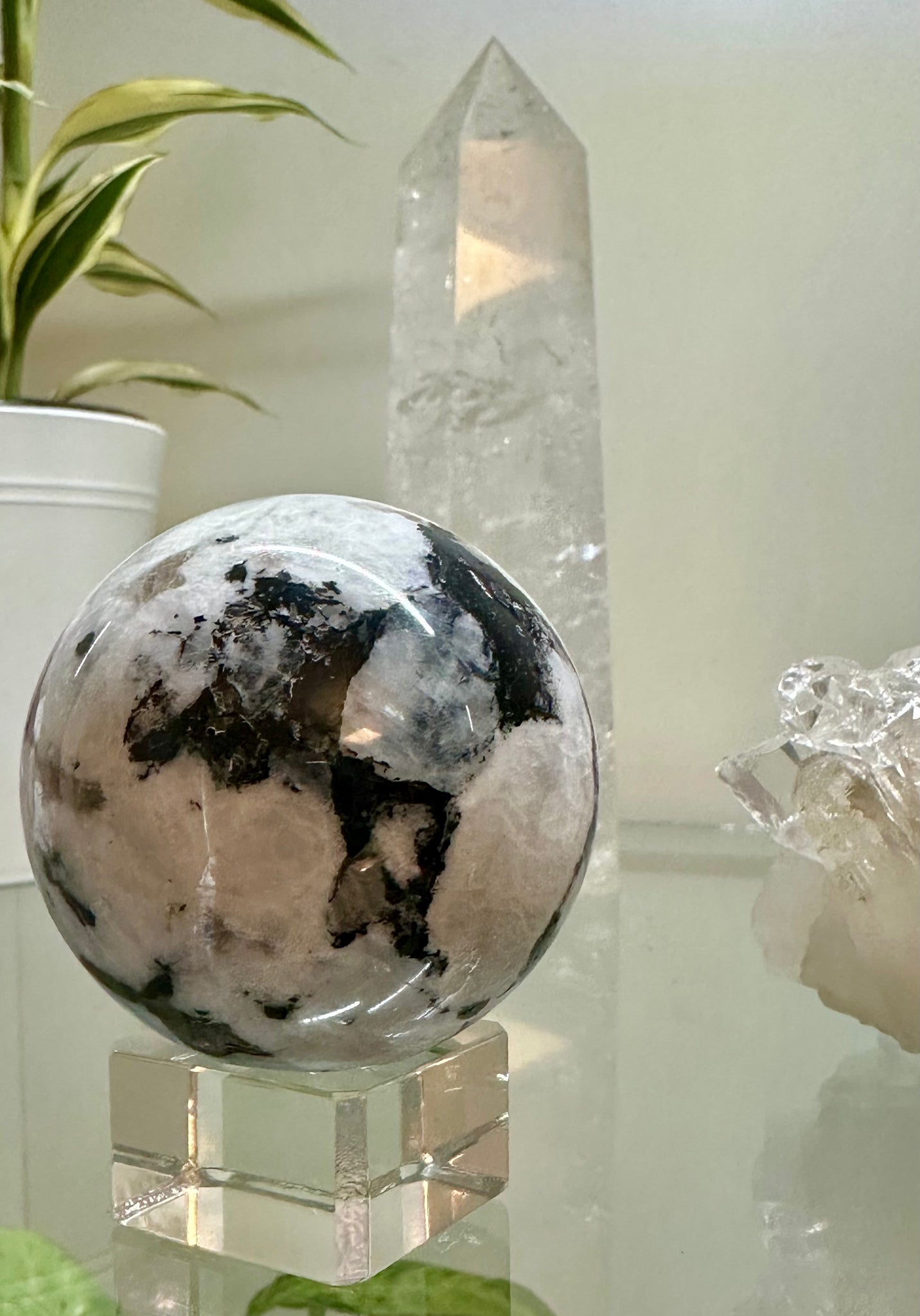 Kelowna Crystal Cave - A polished Rainbow Moonstone sphere displayed on a clear stand, with a crystal in the background.
