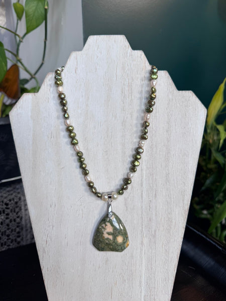 My Two Daughters Jewelry - A beaded necklace with olive green and white beads and a teardrop-shaped green stone pendant, displayed on a white jewelry stand.