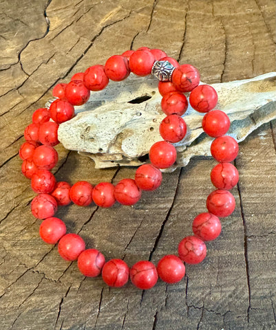 My Two Daughters Jewelry - A red howlite bracelet displayed on a wooden surface, with each bead approximately spherical in shape and the bracelet forming a loop.