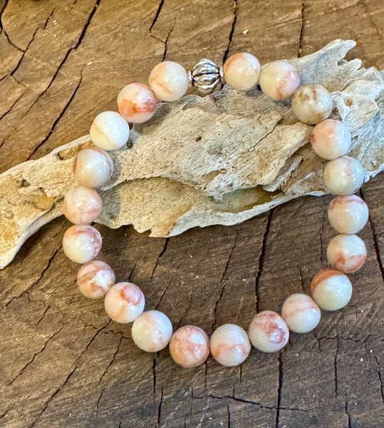 My Two Daughters Jewelry - A Red Vein Jasper bracelet displayed next to a piece of driftwood, with a card describing the stone's properties and meaning.