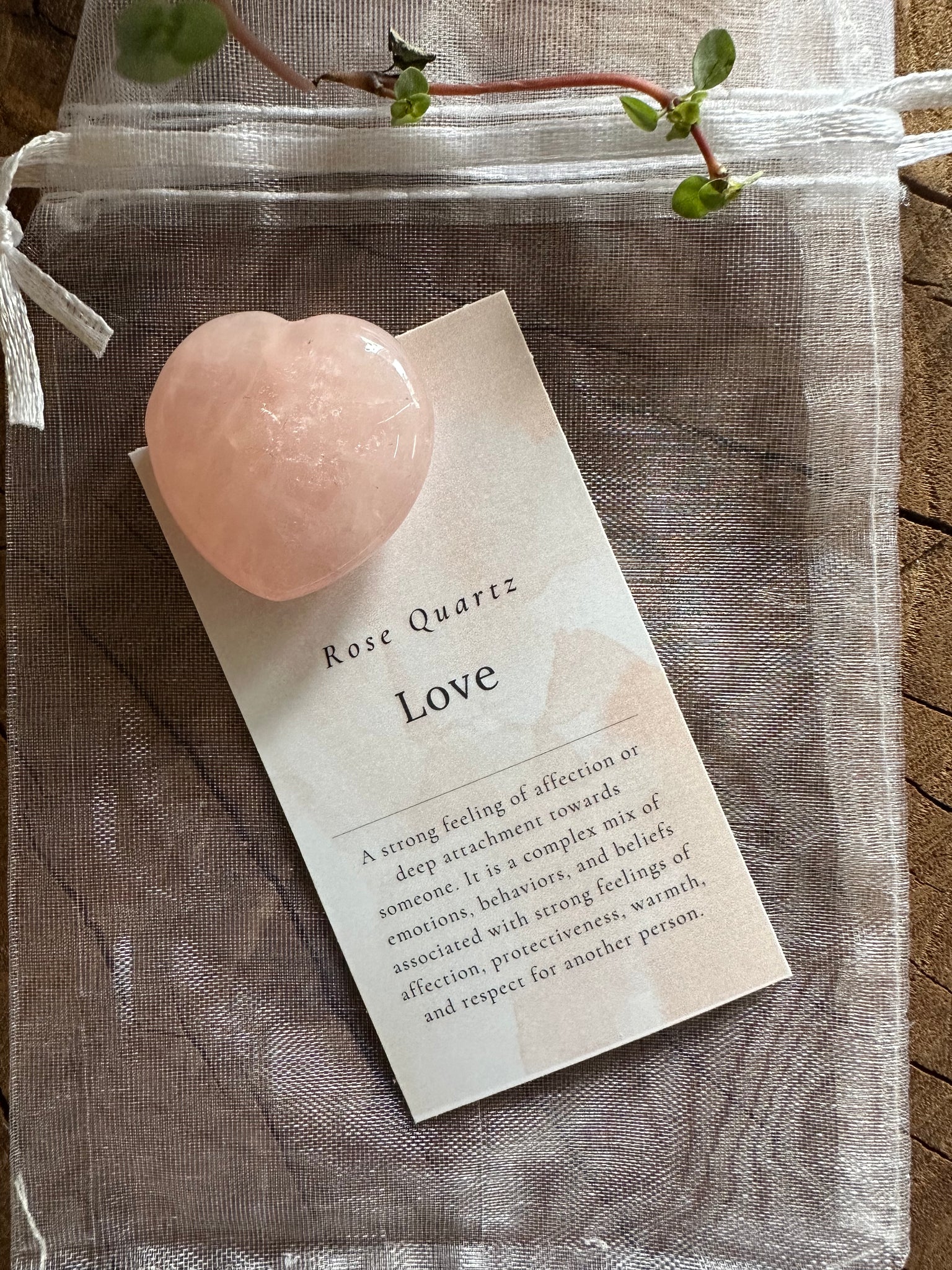 Kelowna Crystal Cave - A polished rose quartz heart crystal with a note and organza bag on a wooden surface.