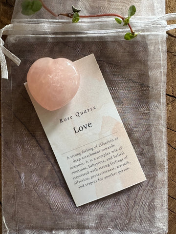 Kelowna Crystal Cave - A polished rose quartz heart crystal with a note and organza bag on a wooden surface.