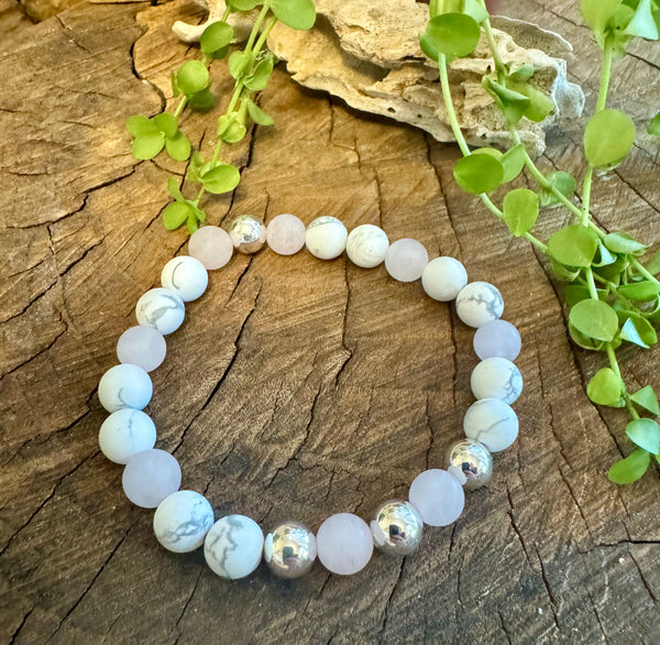 My Two Daughters Jewelry - A bracelet made of matte rose quartz and howlite beads displayed on a wooden surface with green leaves in the background.