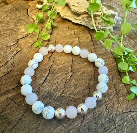 My Two Daughters Jewelry - A bracelet made of matte rose quartz and howlite beads displayed on a wooden surface with green leaves in the background.