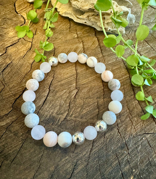 My Two Daughters Jewelry - A bracelet made of matte rose quartz and zebra jasper beads displayed on a wooden surface with green leaves in the background.