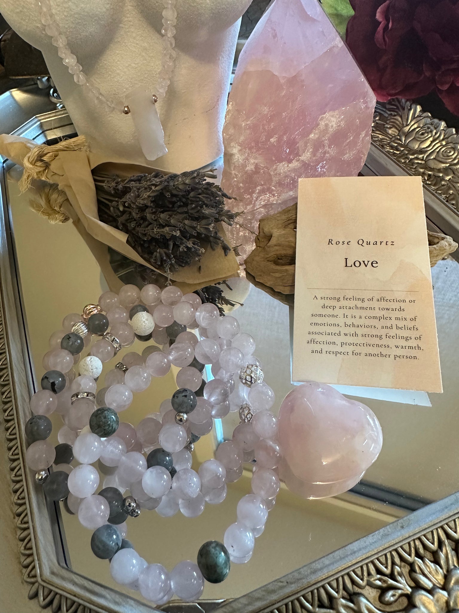My Two Daughters Jewelry - The image shows a bracelet made of rose quartz and labradorite beads displayed alongside a piece of crystal quartz, a small labradorite stone, and a card with the word 'Love' written on it, all arranged on a reflective surface.