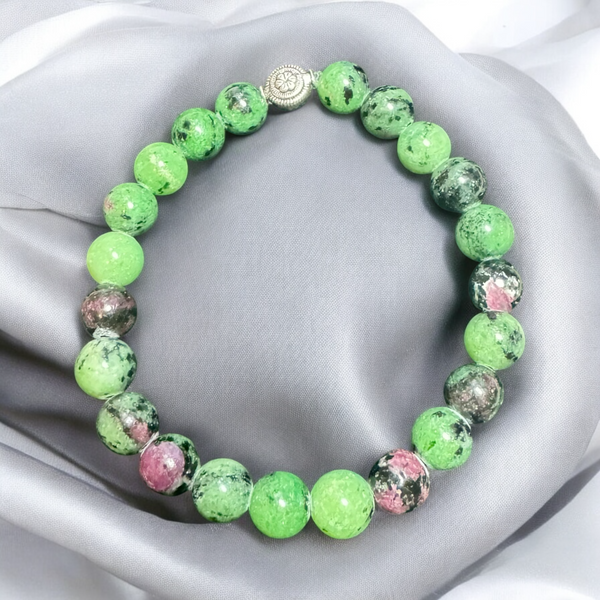 My Two Daughters Jewelry - A beaded bracelet with green and black patterns, featuring metallic silver accents, displayed on a silky gray background.