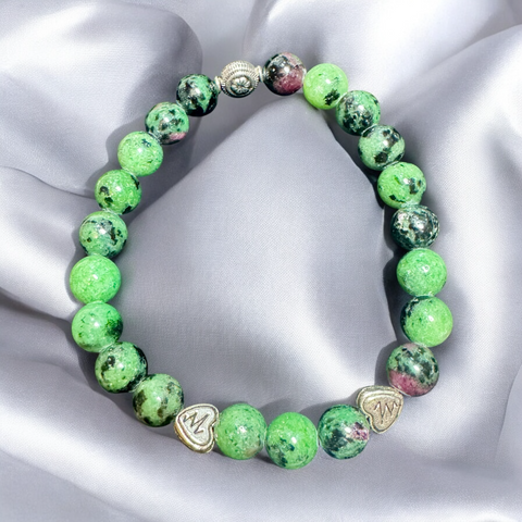 My Two Daughters Jewelry - A beaded bracelet with green and black patterns, featuring metallic silver heart accents, displayed on a silky gray background.