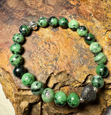 My Two Daughters Jewelry - A bracelet with green and black beads, possibly made of ruby zoisite and lava stone, displayed on a rocky surface.
