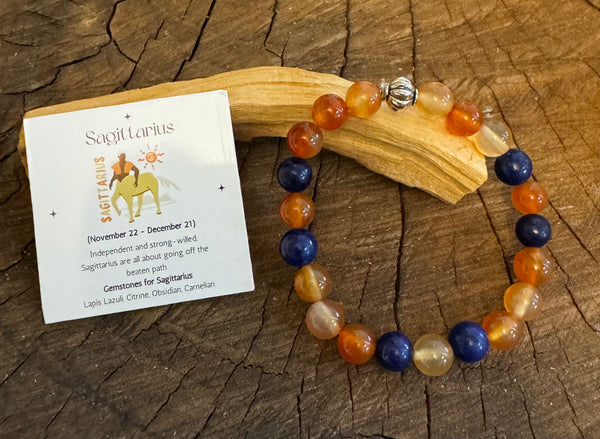 My Two Daughters Jewelry - A two-tone Sagittarius-themed bracelet with lapis and carnelian beads, accompanied by a card with zodiac information placed on a wooden surface.