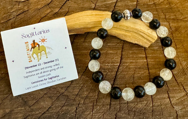 My Two Daughters Jewelry - A two-tone Sagittarius-themed bracelet with black and citrine beads, accompanied by a card with zodiac information placed on a wooden surface.