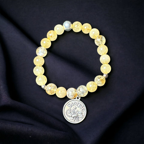 My Two Daughters Jewelry - A bracelet with round yellow beads and a silver-colored Scorpio zodiac sign charm, displayed on a black fabric background.