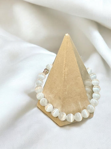 My Two Daughters Jewelry - A white selenite bracelet displayed on a triangular stand against a white fabric background.