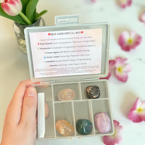 Kelowna Crystal Cave - Self-love crystal box with stones and information card, held by a hand with flowers in the background.